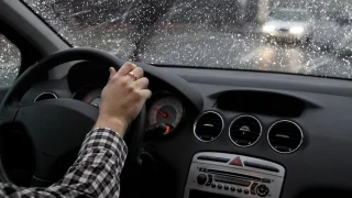 person driving in rain with both hands on steering wheel